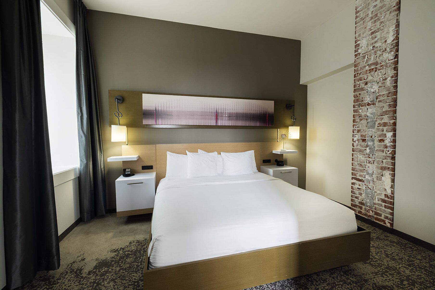 A hotel room with a large bed, two bedside tables, a wall-mounted artwork, and a brick accent wall.