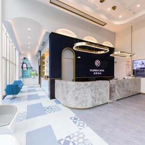 Ein Hotel-Rezeptionsbereich mit Marmor-Theke, blauer Sitzgelegenheit und einem modernen Kronleuchter.