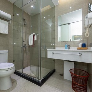 Ein modernes Badezimmer mit einer Duschkabine, einer weißen Toilette, einem Waschbecken mit Spiegel und einem roten Korb.