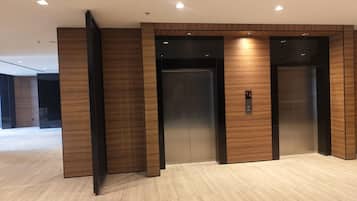 A modern elevator with a metallic finish, flanked by wooden paneling, in a spacious, well-lit lobby area.