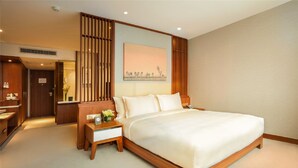 A hotel room with a large bed, wooden headboard, a nightstand with a lamp, a desk, and a painting on the wall. - Deacon House Wuxi (Wuxi)