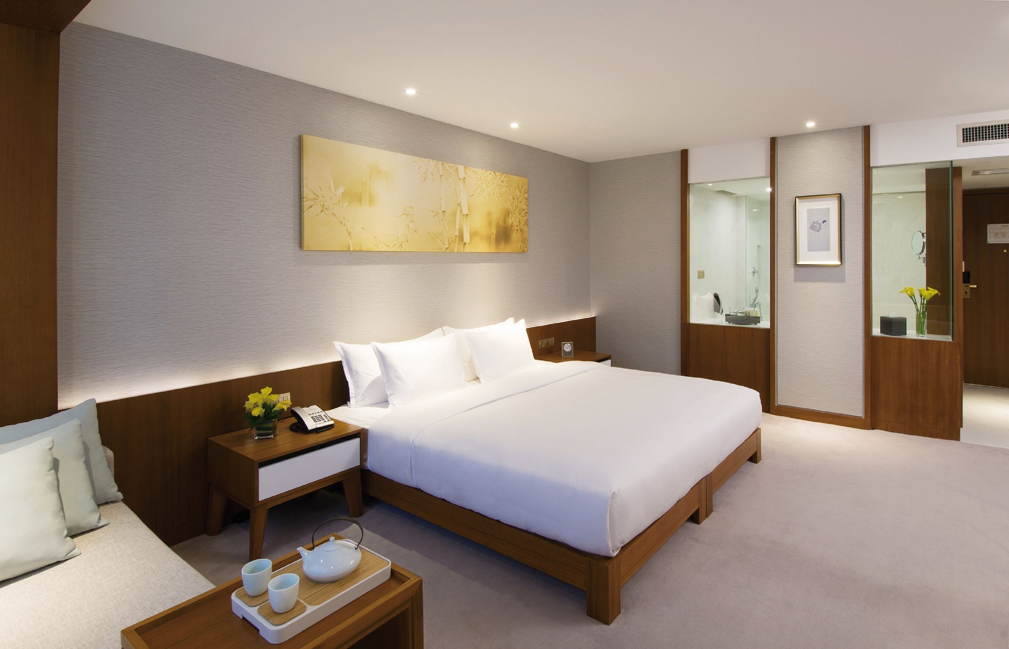 Una habitación de hotel moderna con una cama grande, mesitas de noche, un armario de madera y una obra de arte colgada en la pared.