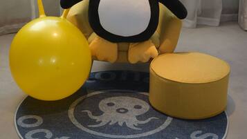 Un jouet en peluche représentant un pingouin, avec un ballon jaune et un coussin rond, posé sur un tapis rond orné d’un motif circulaire.