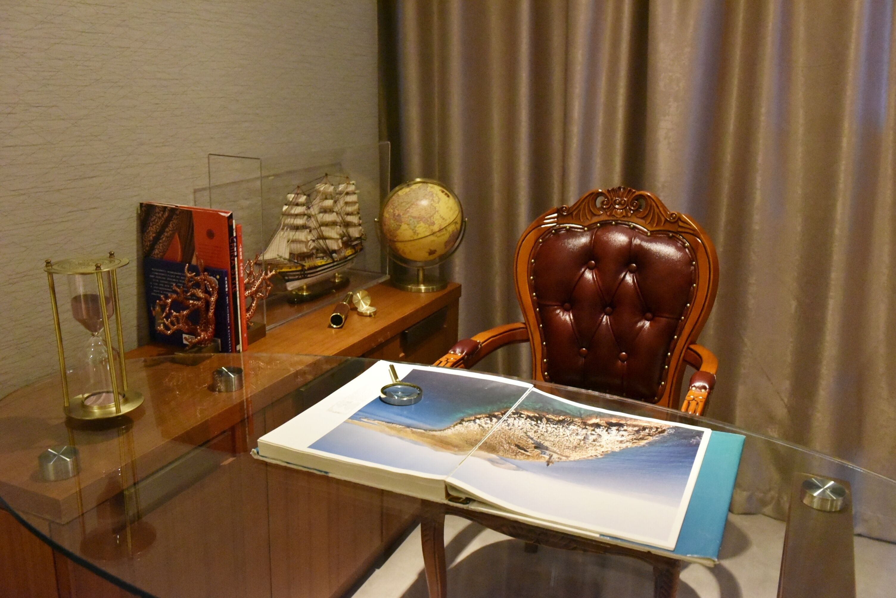 A glass table with a map, a globe, and a ship model.
