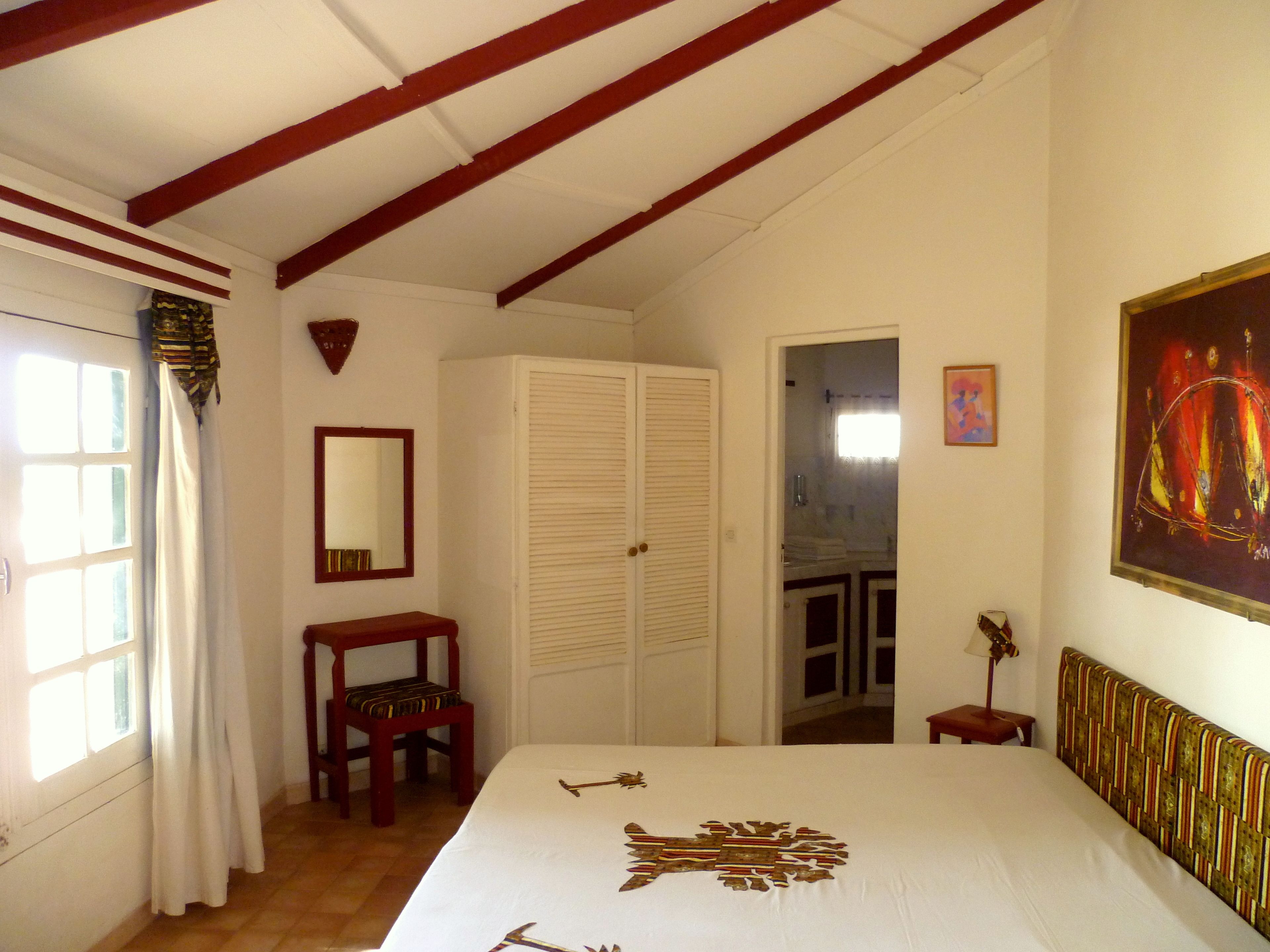 A bedroom with a bed, a wooden chair, a wardrobe, a mirror, and a painting on the wall.