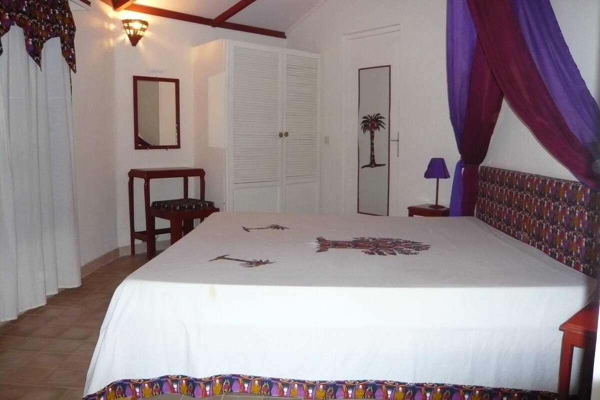 A bedroom with a bed, a nightstand, a chair, a wardrobe, and a door with a palm tree design.