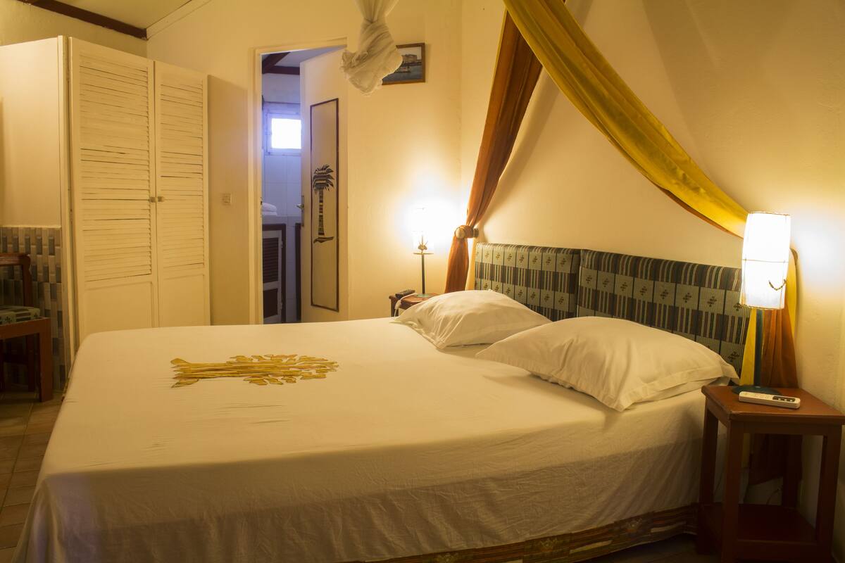A neatly made bed with white linens and a decorative golden pattern, a bedside lamp, and a wooden nightstand.