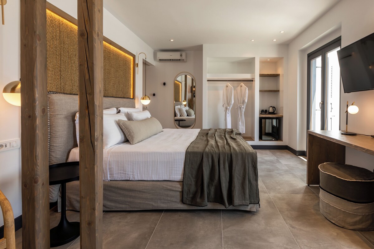 A modern bedroom with a large bed, a desk, a mirror, and a TV.