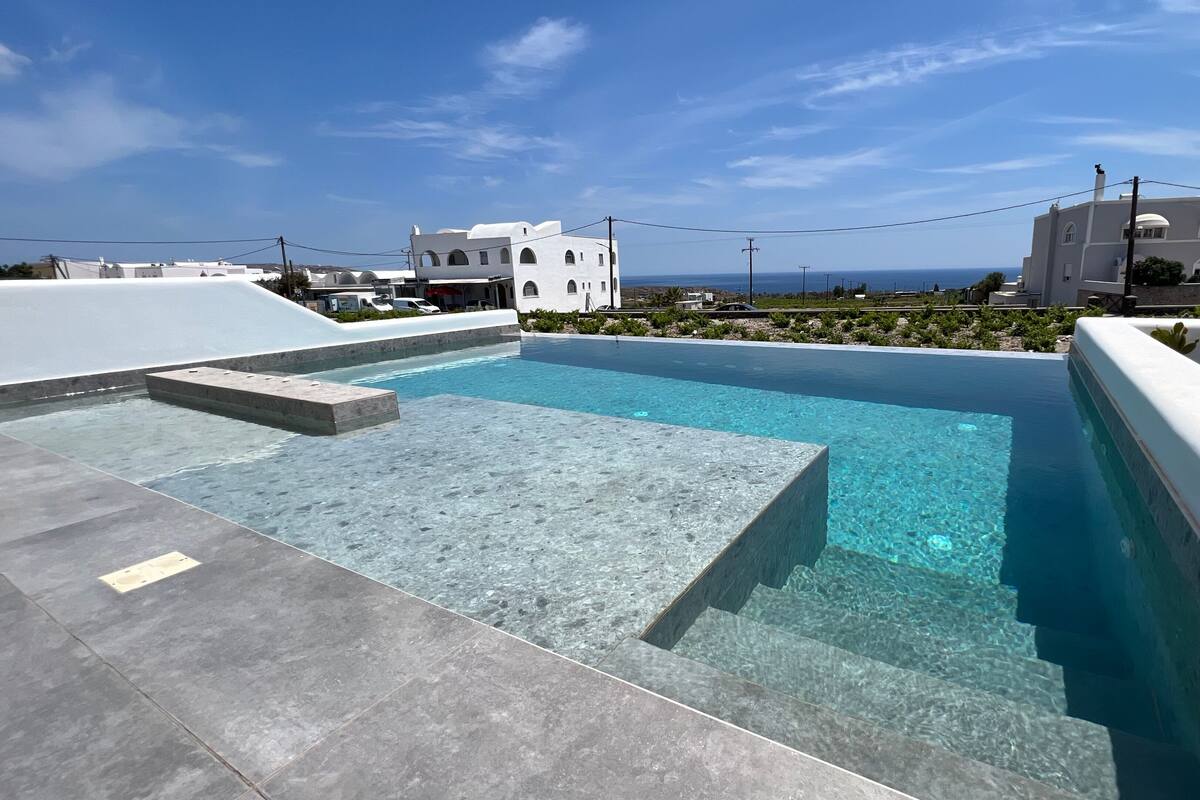 A rooftop pool with clear blue water, surrounded by a modern architectural setting and a view of the sea.