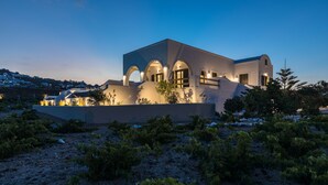 A modern building with arched windows and a flat roof, surrounded by a landscaped area with shrubs. - Vineyard Exclusive Suites (Santorini)