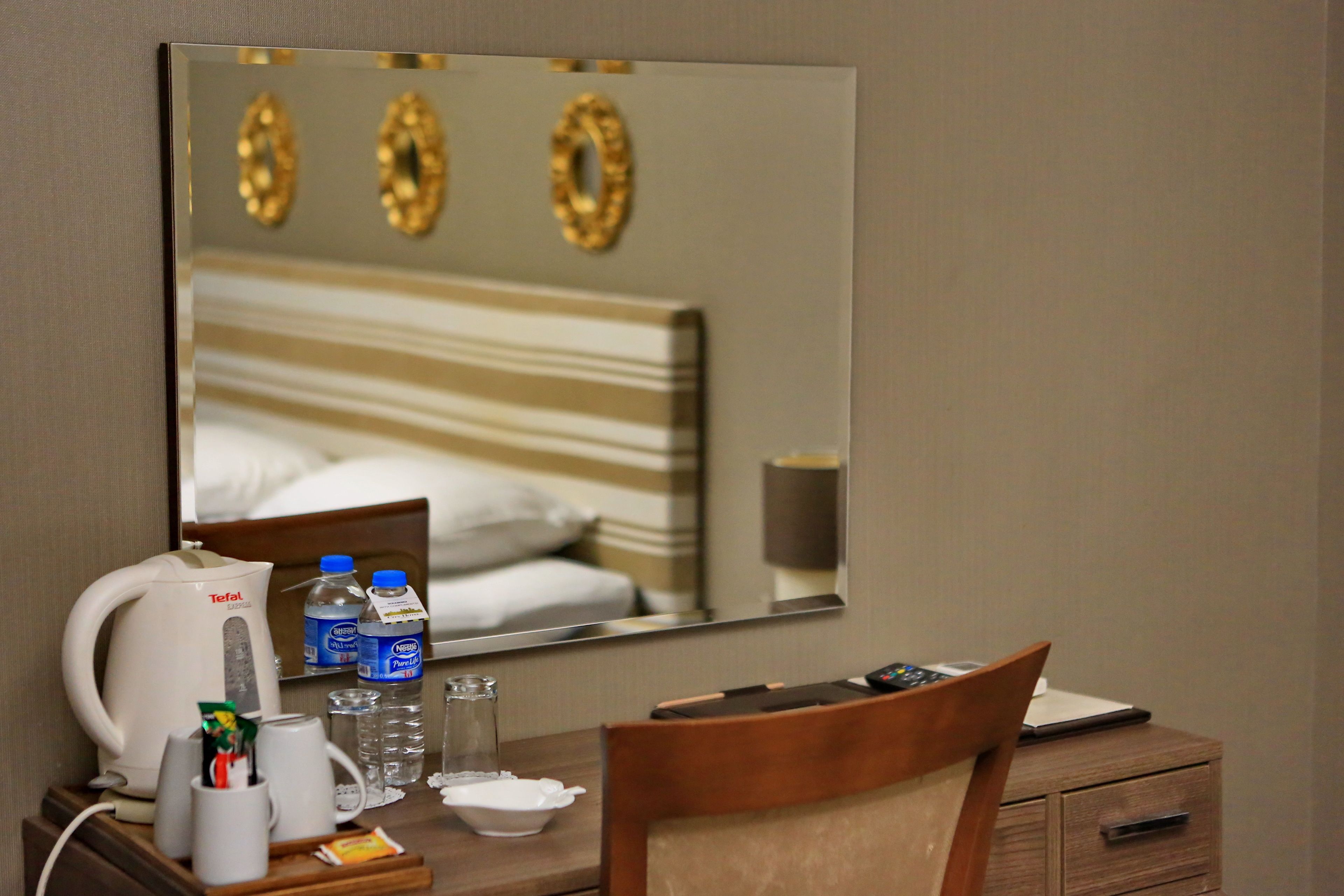Habitación de hotel con cama, mesita de noche con hervidor, botellas de agua, vaso, taza y silla.