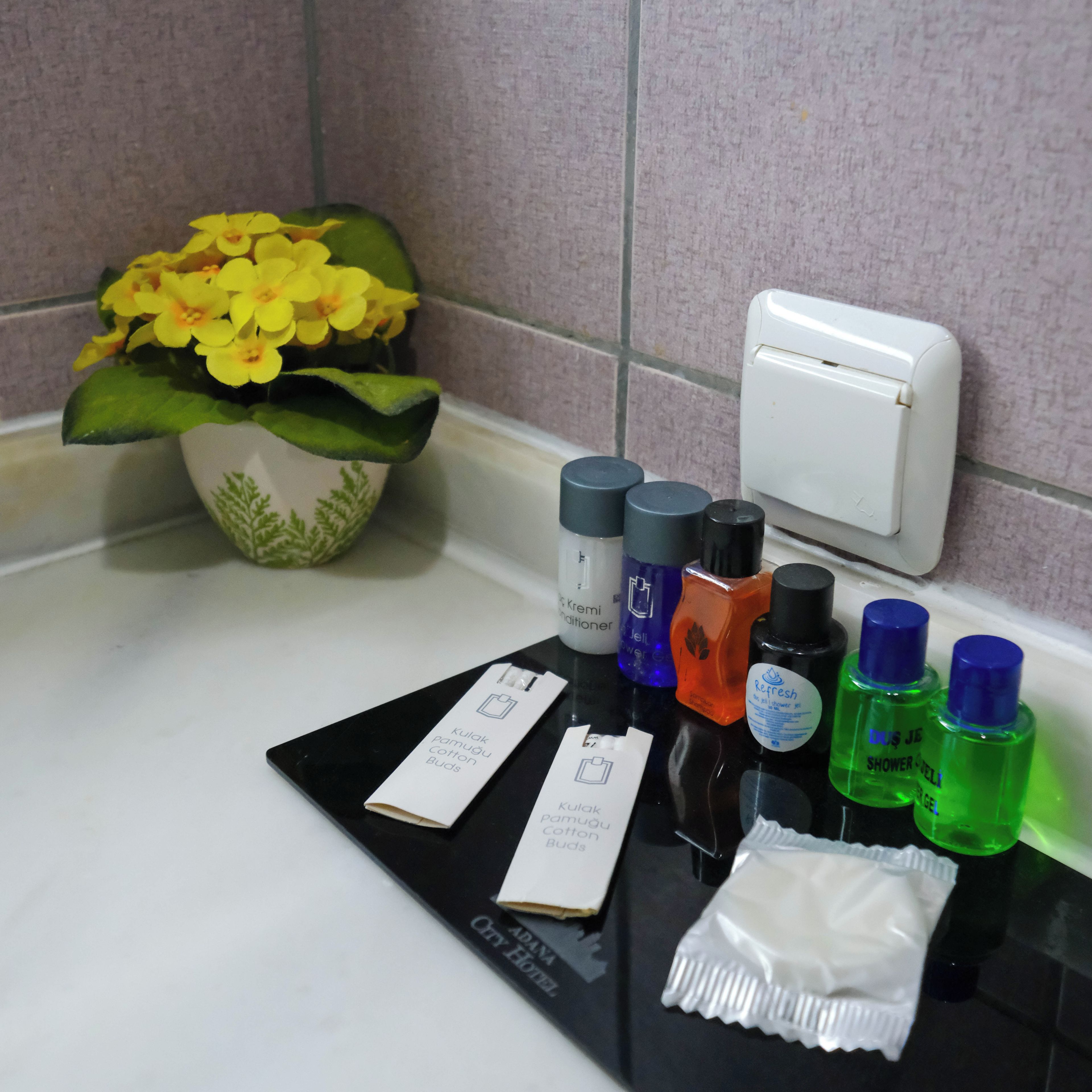 Una encimera de baño con artículos de aseo, un florero y un secador de manos.