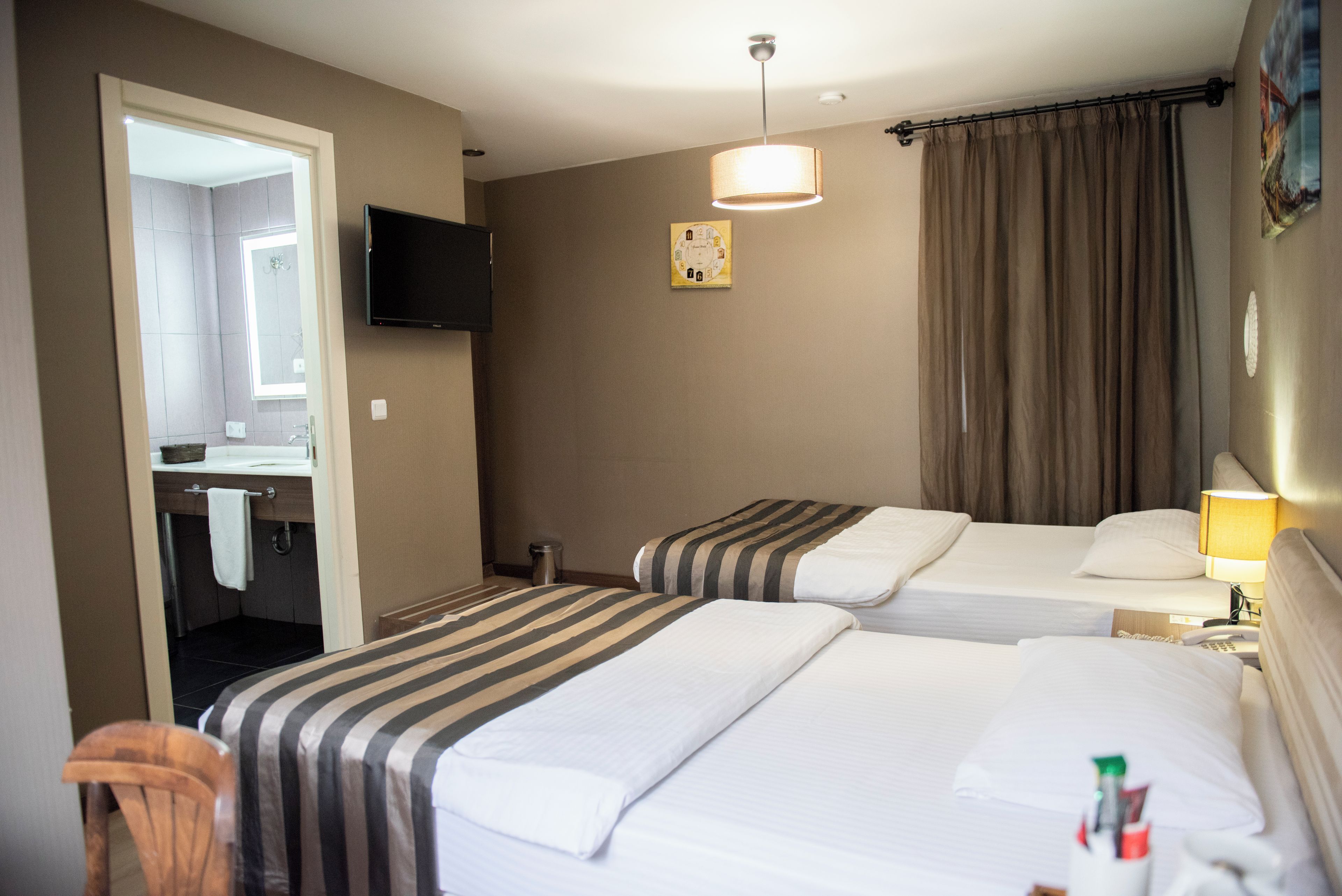 Une chambre d’hôtel avec deux lits, une télévision, une horloge et une salle de bain visible à travers une porte ouverte.