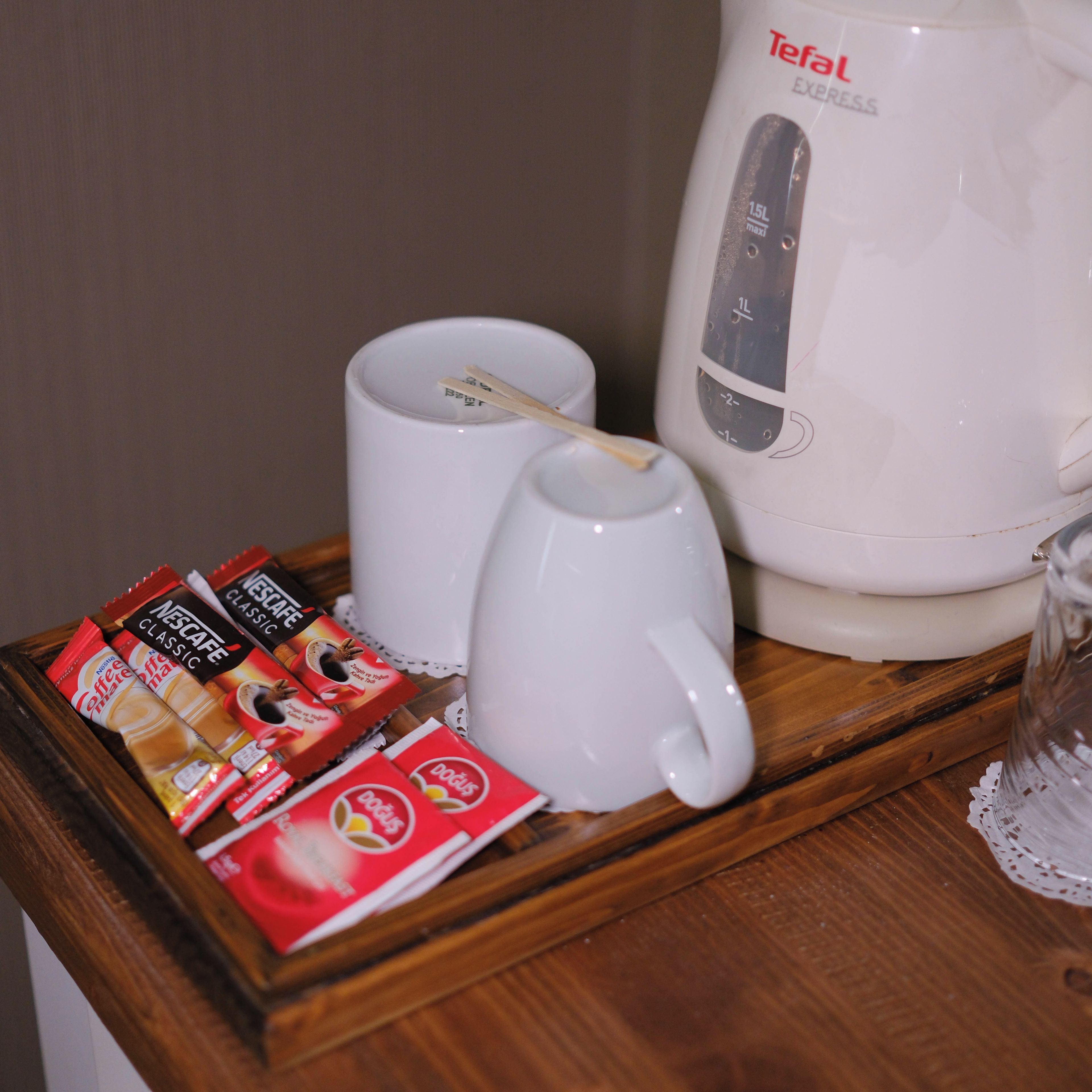 Una cafetera, dos tazas y sobres de café sobre una superficie de madera.