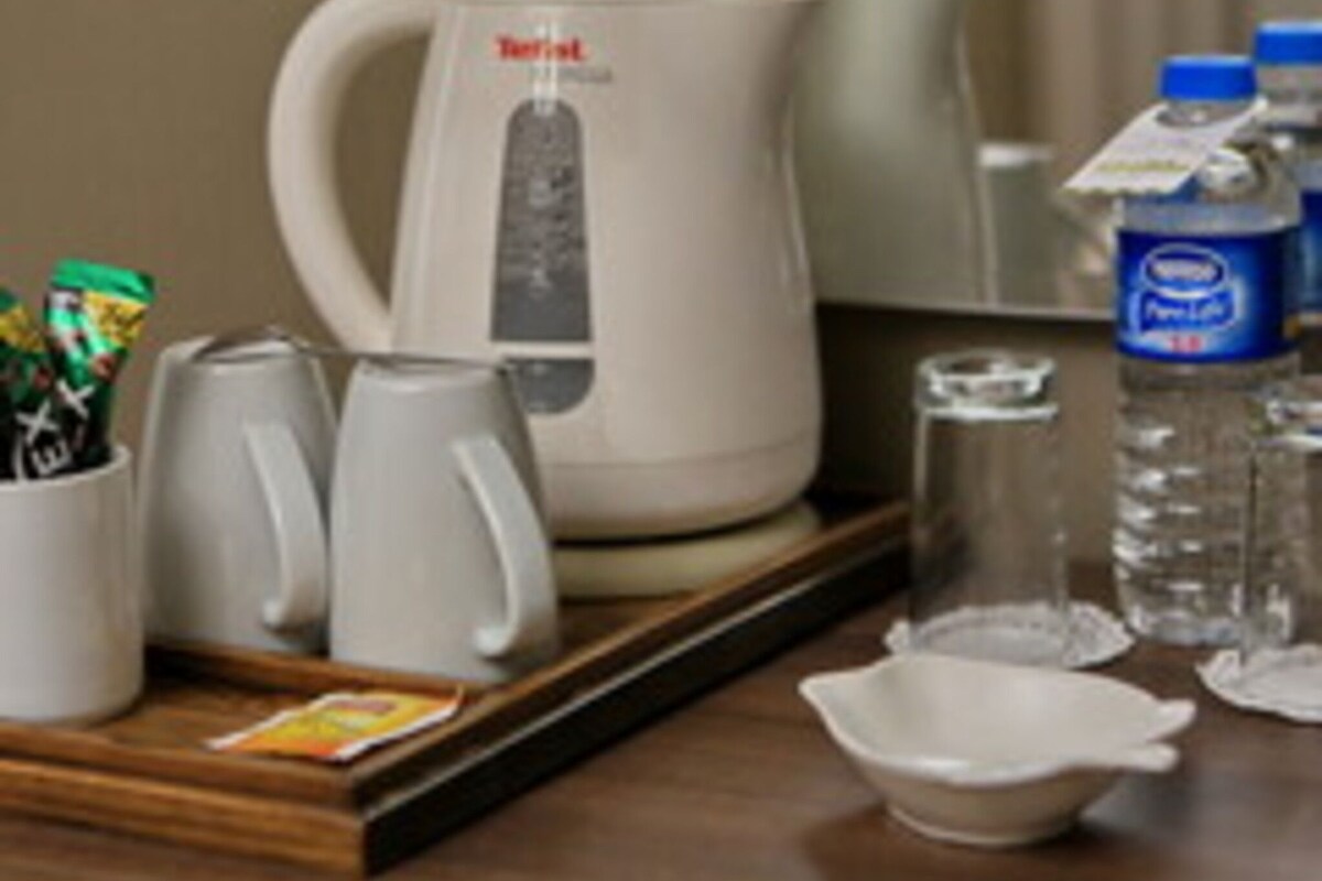 A hotel room with a coffee maker, two cups, a tray, a bottle of water, and a glass.