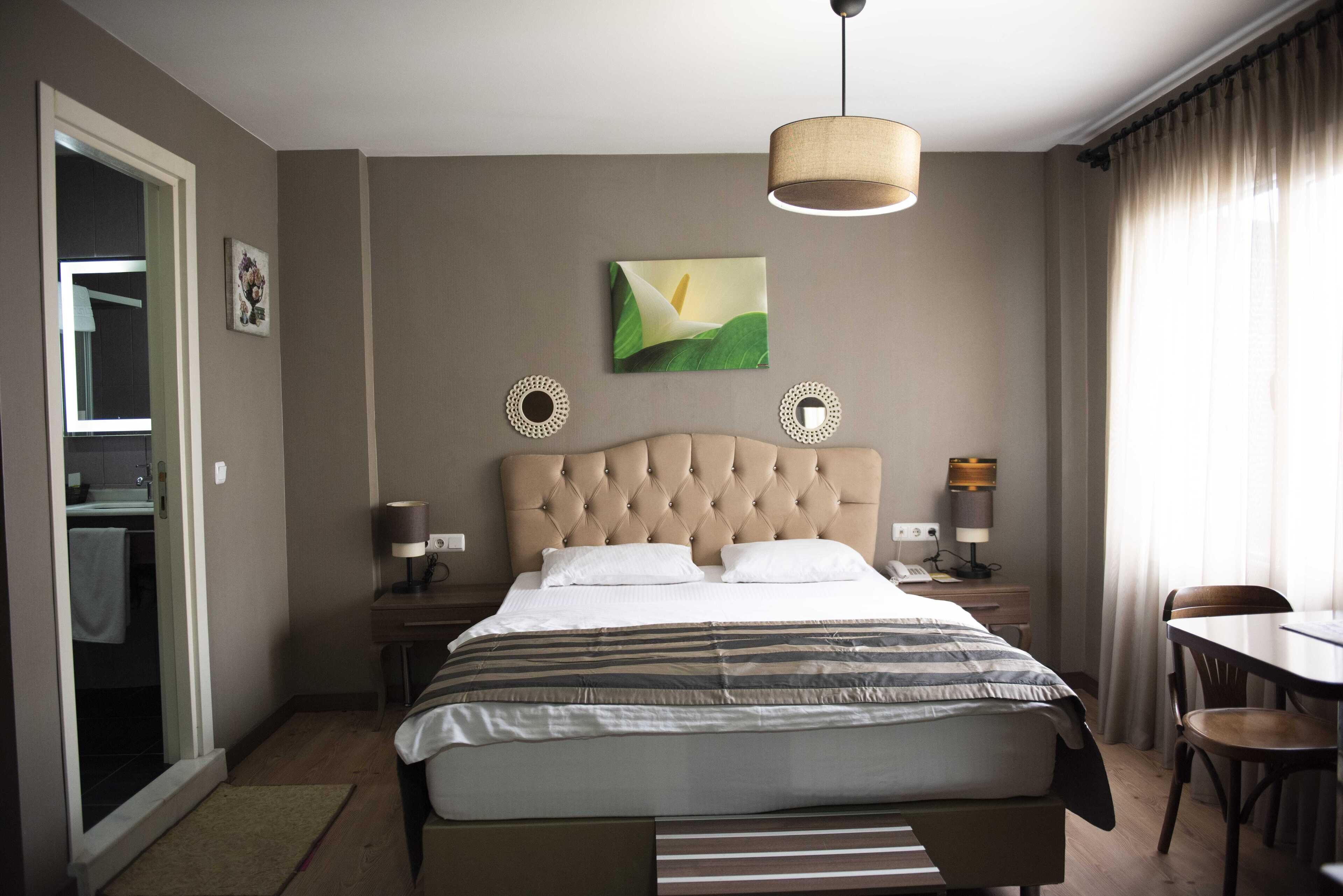 Habitación de hotel con una cama grande, una mesita de noche con lámpara, una silla, una pequeña mesa y un cuadro en la pared.