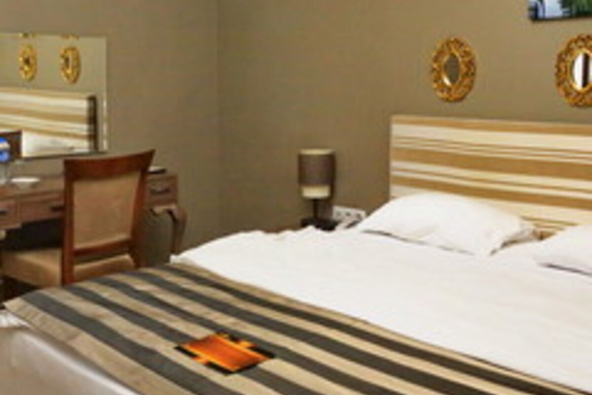 A hotel room with a bed, a desk, a chair, and a painting on the wall.
