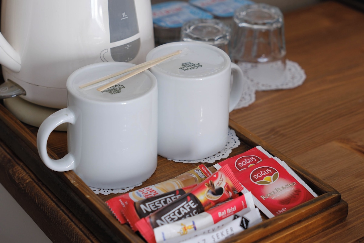 Una bandeja con una tetera Express Tefal, dos tazas blancas y sobres de café Nescafé y Doğus.