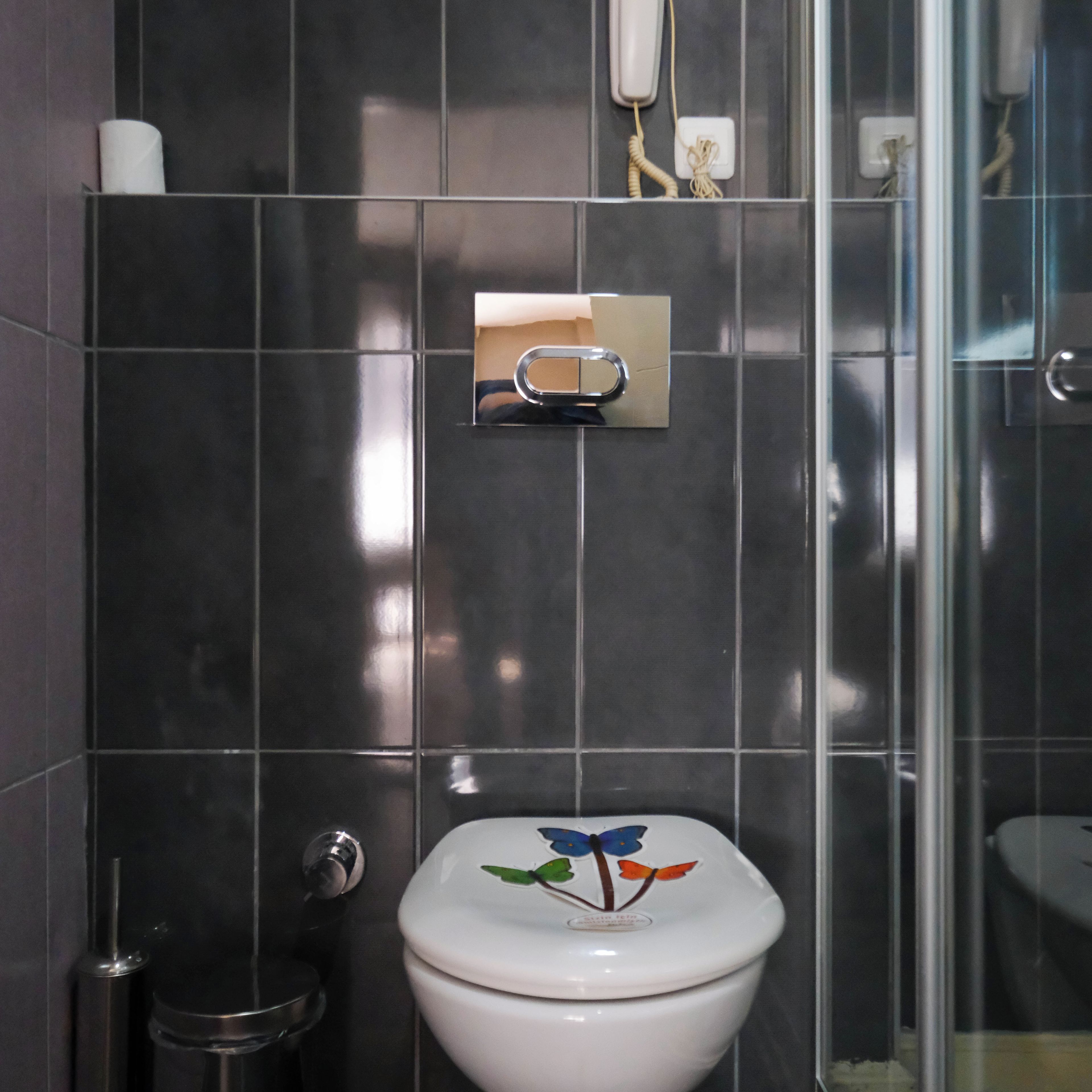 Un bagno moderno con pareti piastrellate di colore scuro, un water con coperchio decorativo, un asciugatore elettrico e un box doccia in vetro.