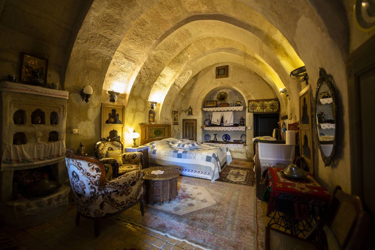 A room with a vaulted ceiling, a bed with a patterned bedspread, a chair, a small table, and a fireplace.