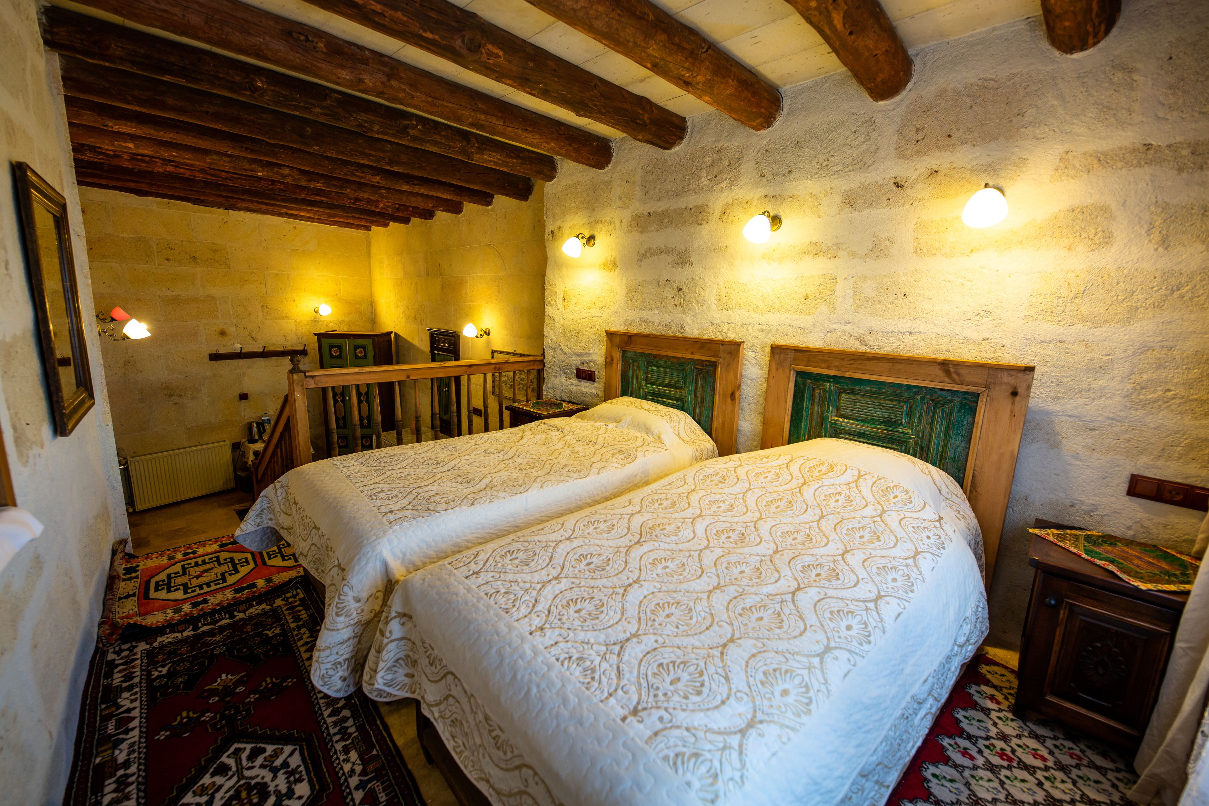 A rustic room with two beds, wooden beams, stone walls, and a small table.