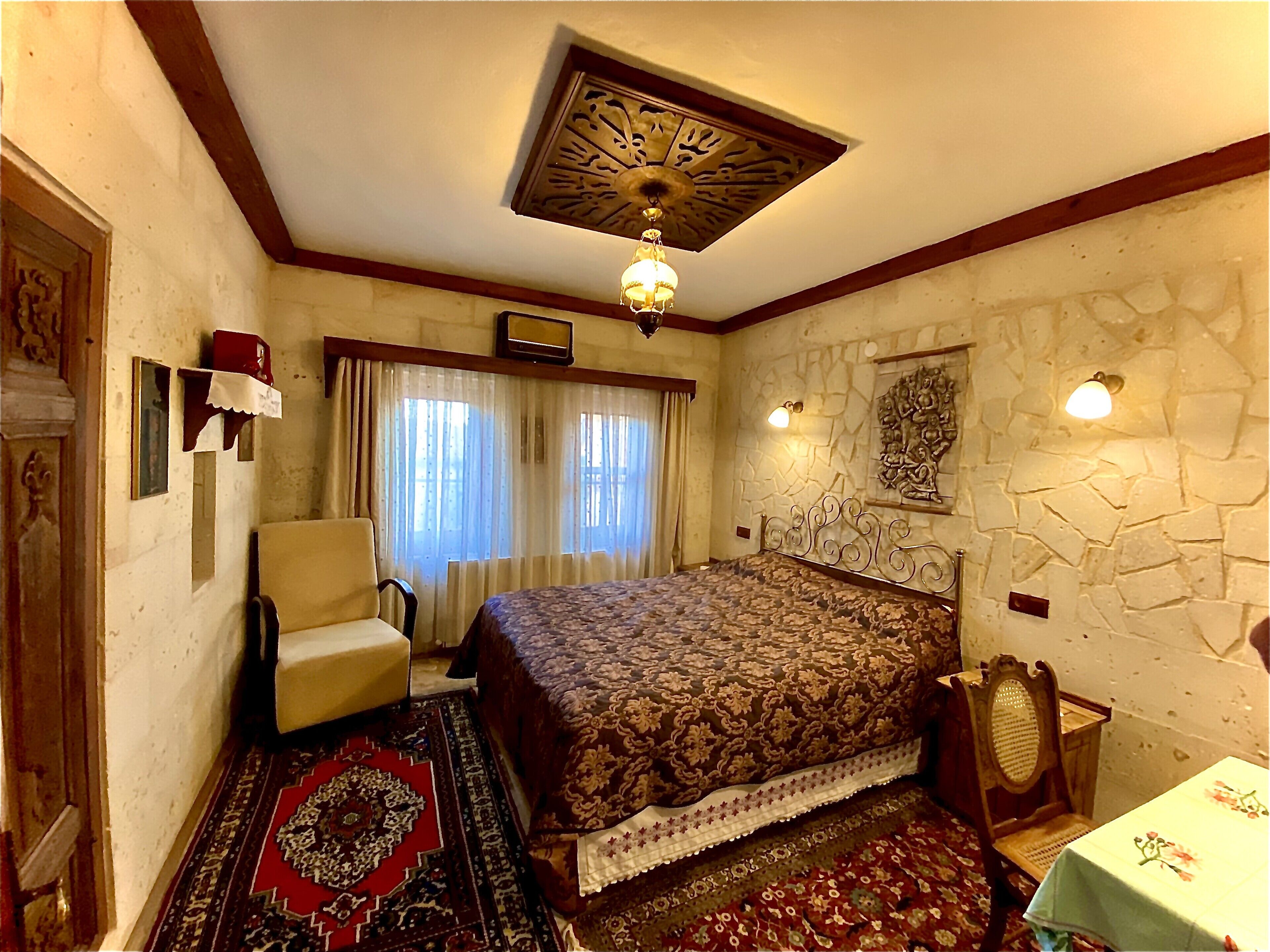 A bedroom with a large bed, a chair, a small table, and a decorative ceiling.