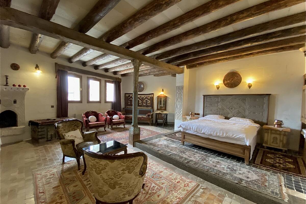 A traditional room with a large bed, wooden beams, a fireplace, and patterned rugs.