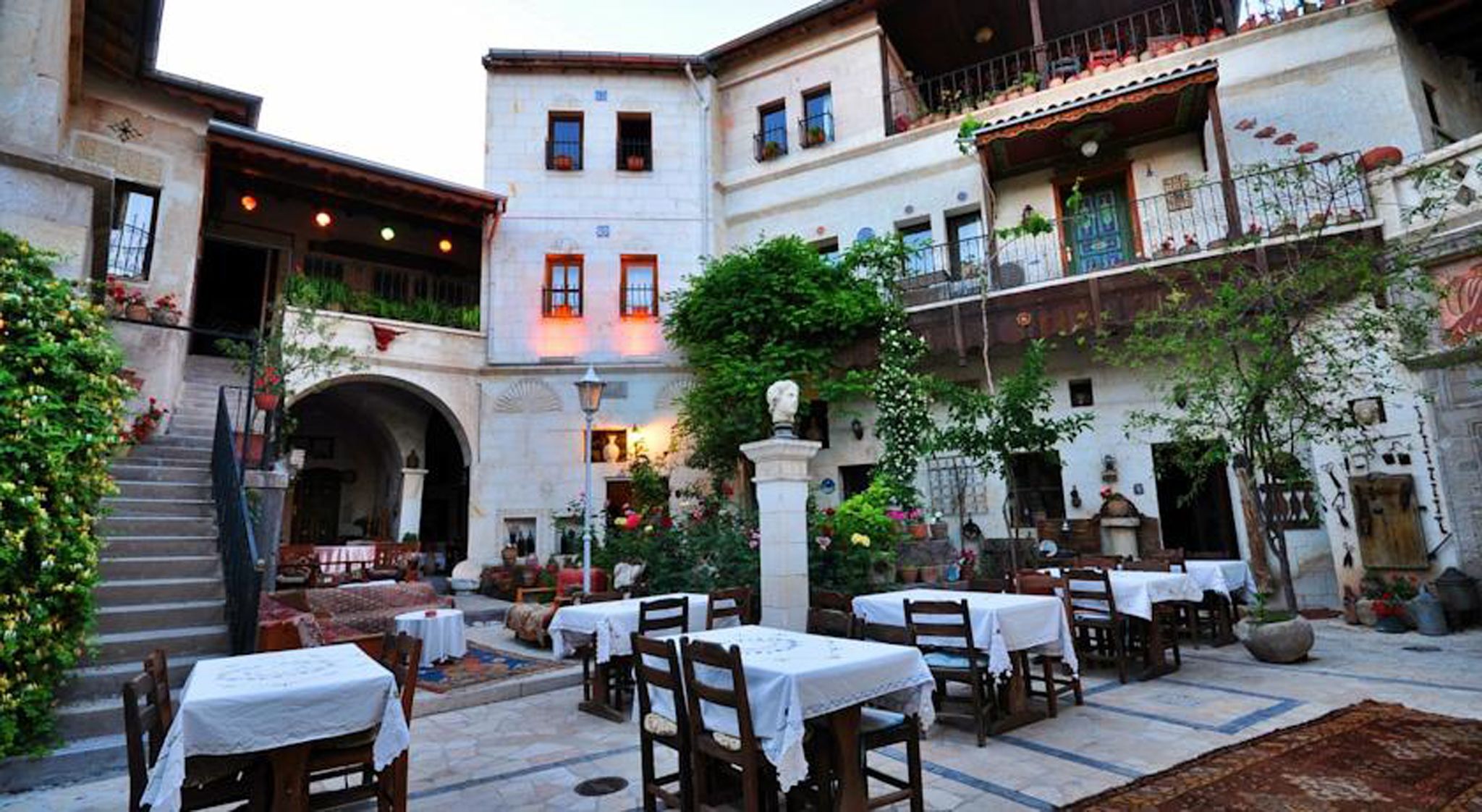 An outdoor courtyard with tables and chairs, a statue, and a building with balconies.