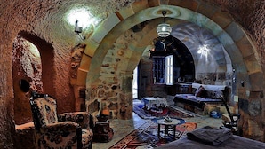 Un interior rústico de piedra con un techo alto y abovedado, un sillón estampado, una mesita y un conjunto de sofás.