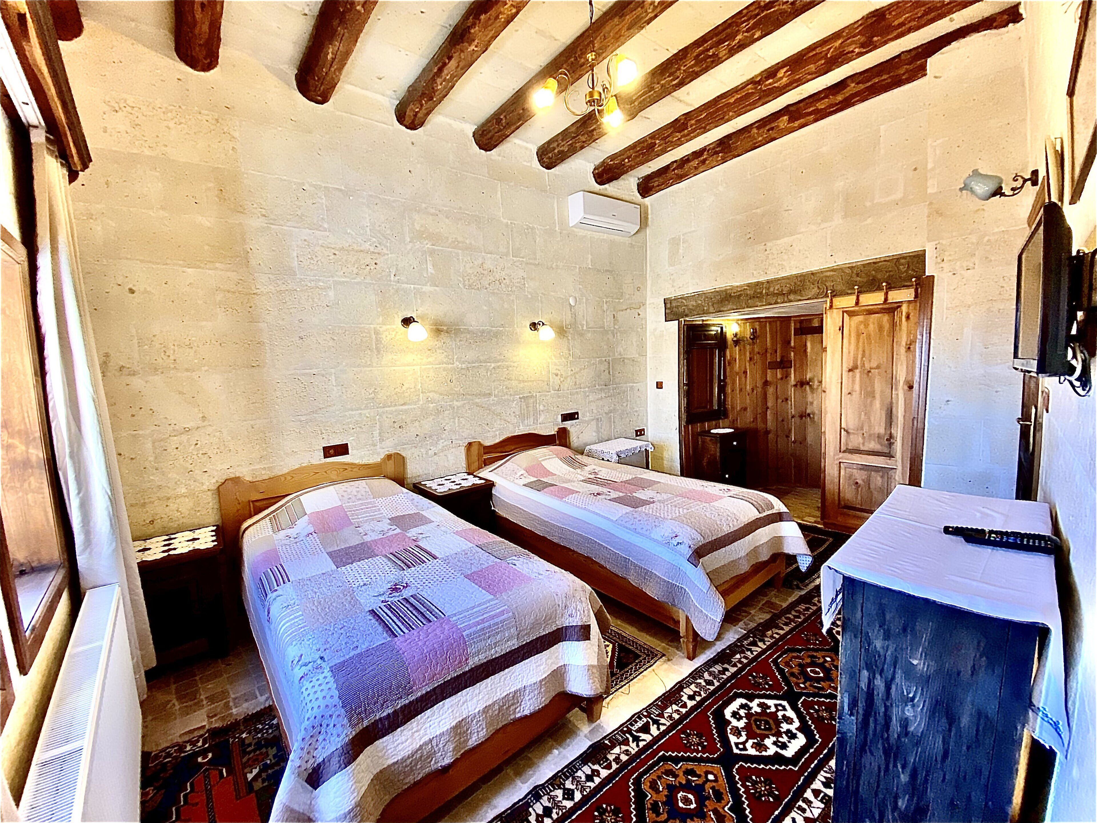 A room with two beds, a wooden ceiling, a wall-mounted air conditioner, a small table, and a television.