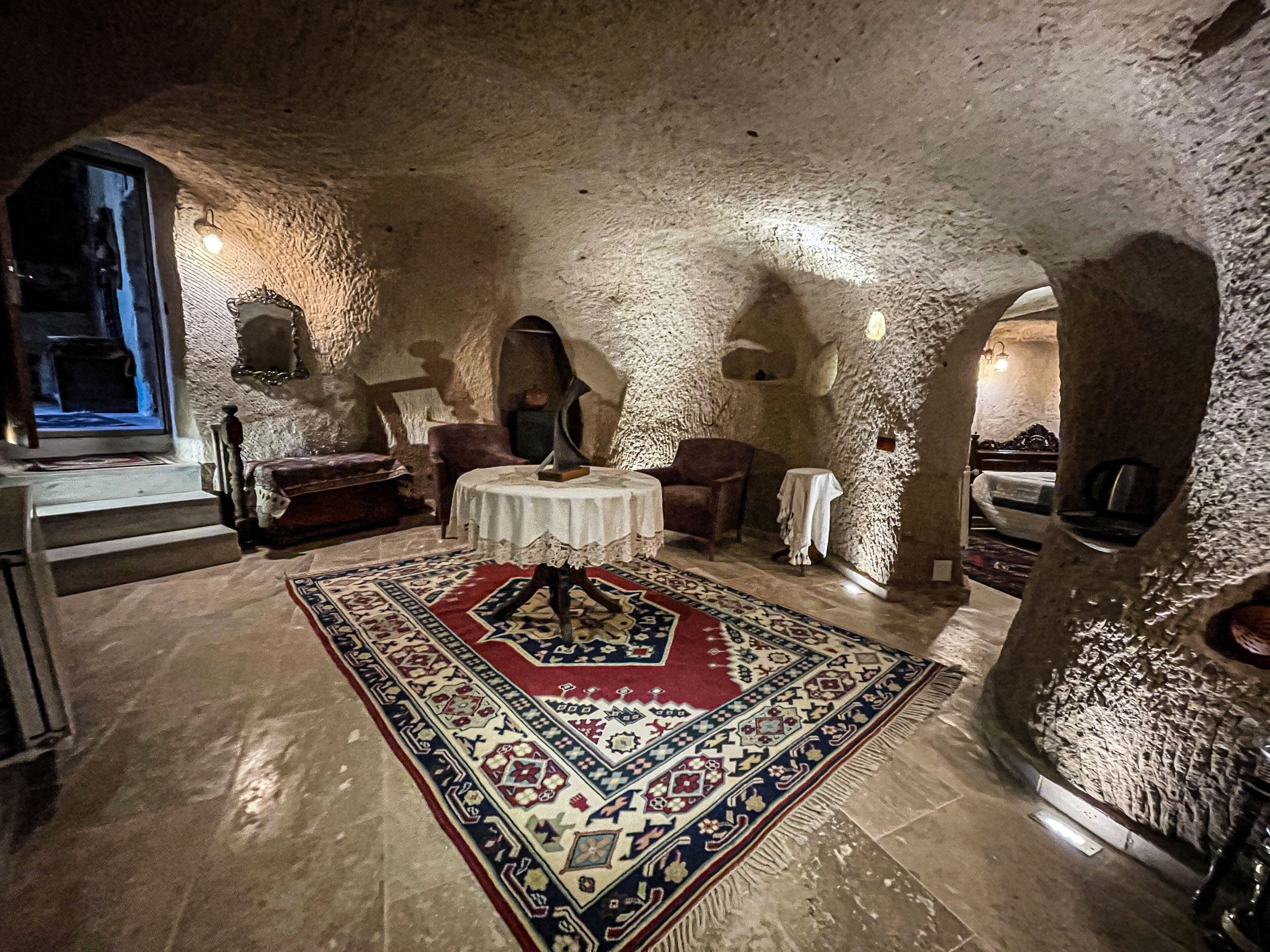 A room with a stone ceiling, a round table with a white tablecloth, a patterned rug, and a window with a view.