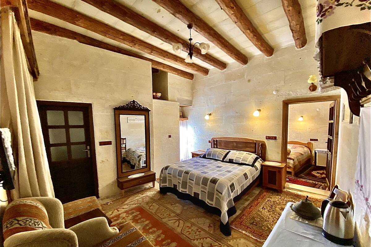 A bedroom with a bed, a mirror, a table with a kettle, and a chair.