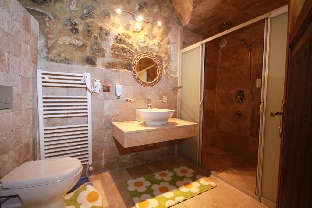 A bathroom with a stone wall, a white toilet, a sink with a mirror, and a shower.