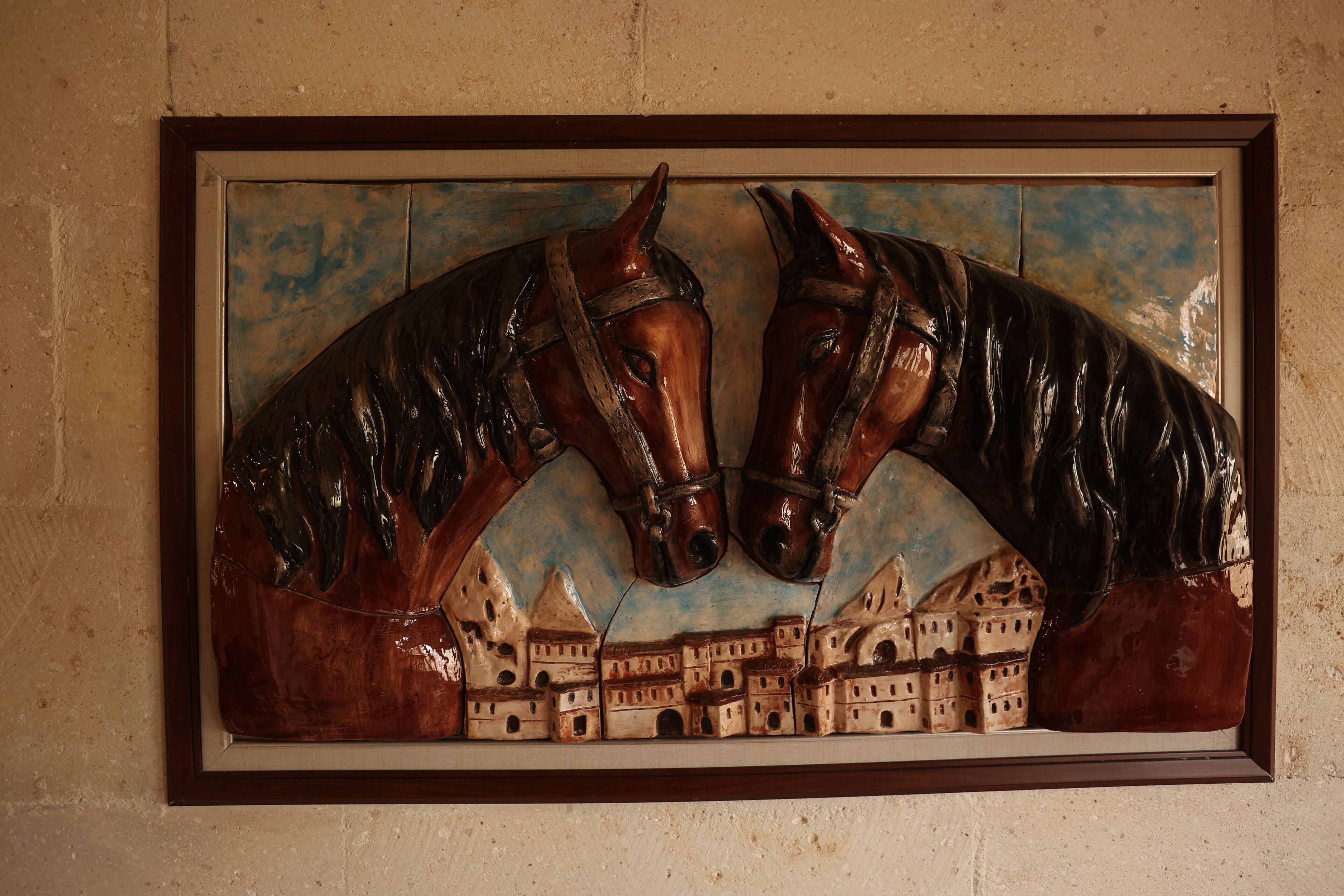 Una escultura en marco que muestra dos caballos con un paisaje urbano al fondo.