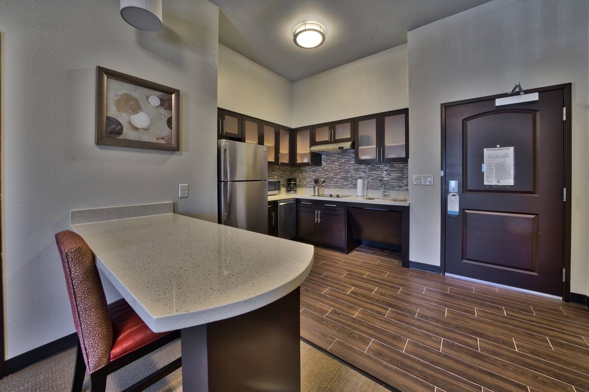A modern kitchen with dark wooden cabinets, a stainless steel refrigerator, and a countertop with a sink.