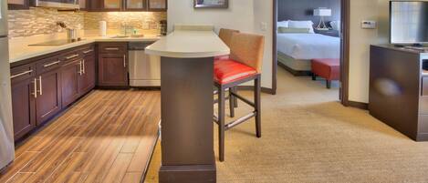 A hotel room with a kitchenette, a bed, a TV, and a bathroom.