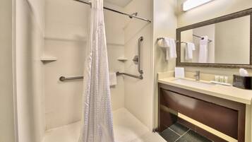 Une salle de bain d’hôtel équipée d’une douche, de barres d’appui, d’un lavabo et d’un miroir.