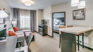 A hotel room with a sofa, a dining table, a TV, and a large window with curtains. - Staybridge Suites Lubbock South by IHG (Lubbock)