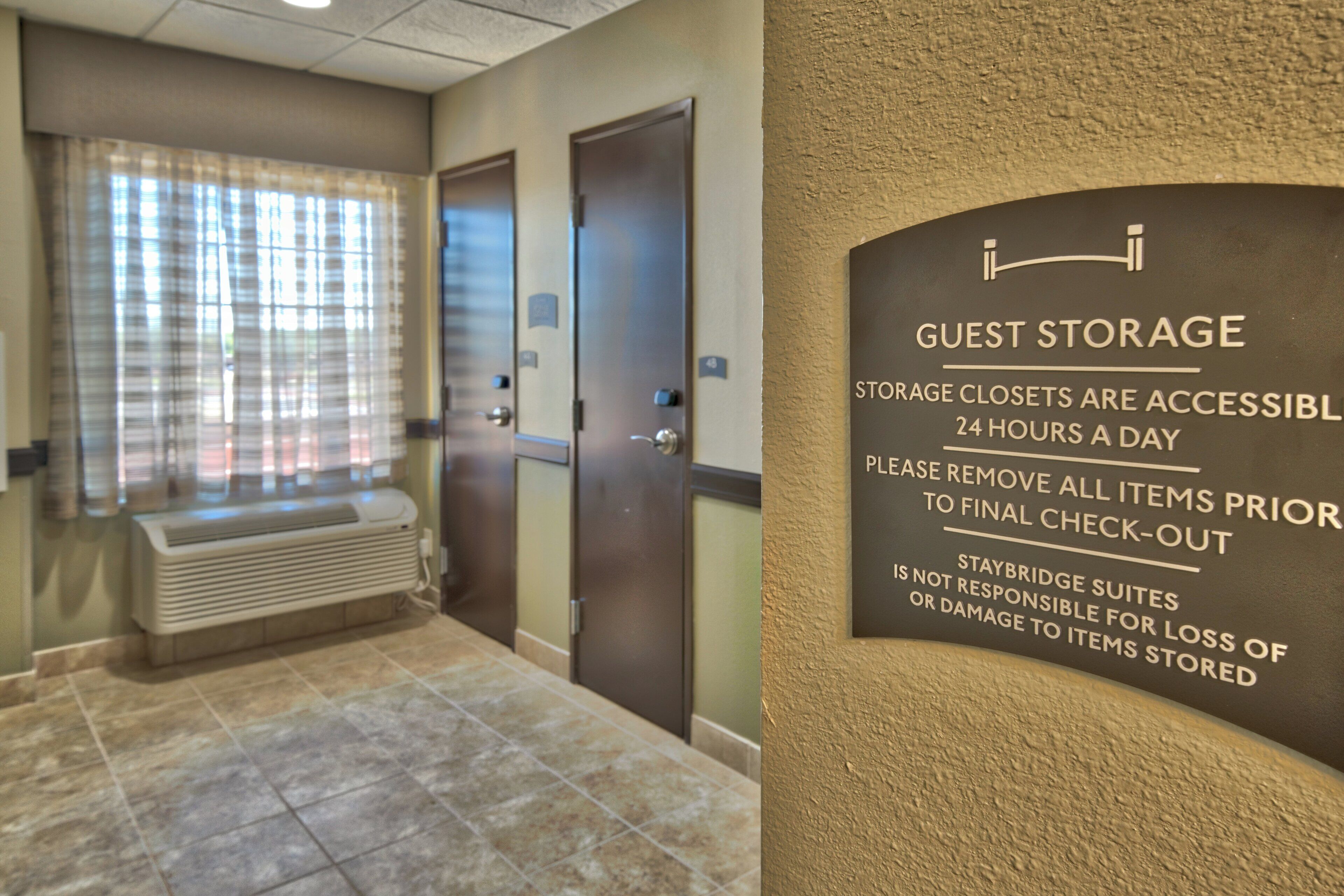 A hotel guest storage area with a sign indicating 24-hour access and a request to remove items prior to check-out.
