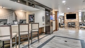A modern kitchen with a bar area, a stone fireplace, and a flat-screen TV mounted on the wall. - Staybridge Suites Lubbock South by IHG (Lubbock)