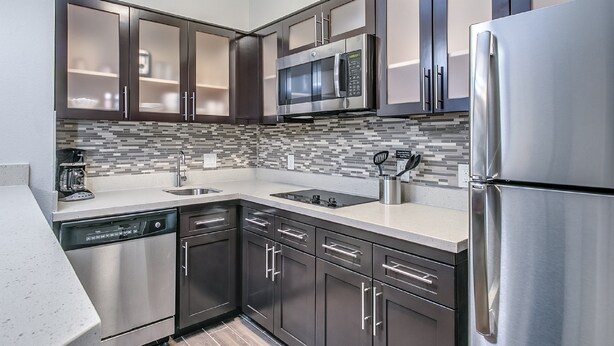 A modern kitchen with stainless steel appliances, dark cabinetry, and a tiled backsplash. - Staybridge Suites Lubbock South by IHG (Lubbock)
