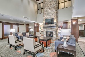 A hotel lobby with a stone fireplace, seating area, and a flat-screen TV mounted on the wall. - Staybridge Suites Lubbock South by IHG (Lubbock)
