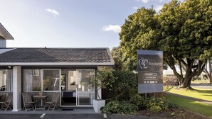 A modern motel with a tiled roof, a patio with chairs and a table, and a signboard advertising a vacancy. - Roselands Motel (Tauranga)