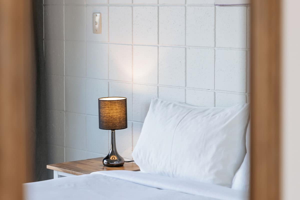 A hotel room with a neatly made bed, a bedside lamp, and a painting on the wall.