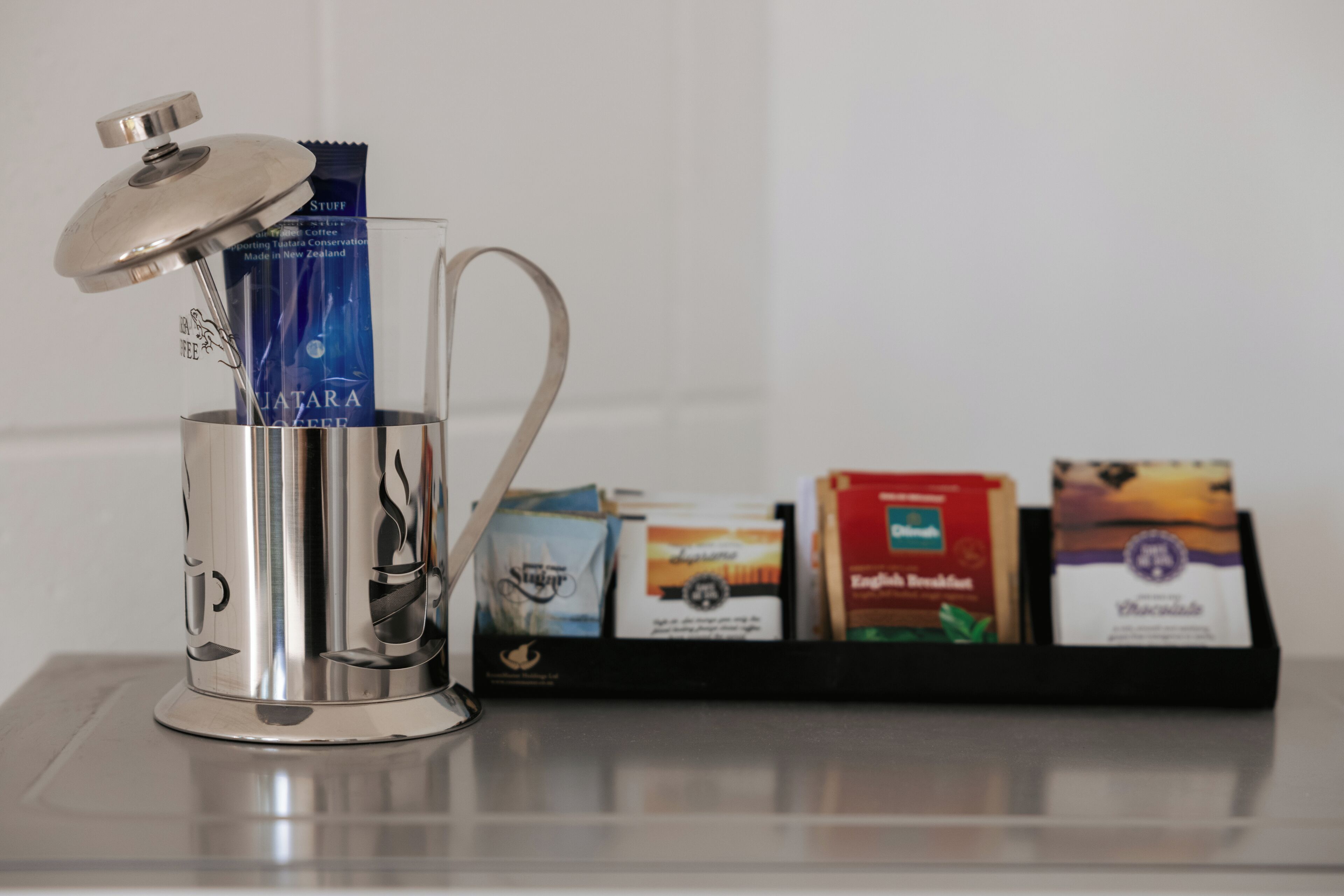 Eine Kaffeemaschine mit Deckel und Tasse, sowie ein Tablett mit Kaffeebeuteln.