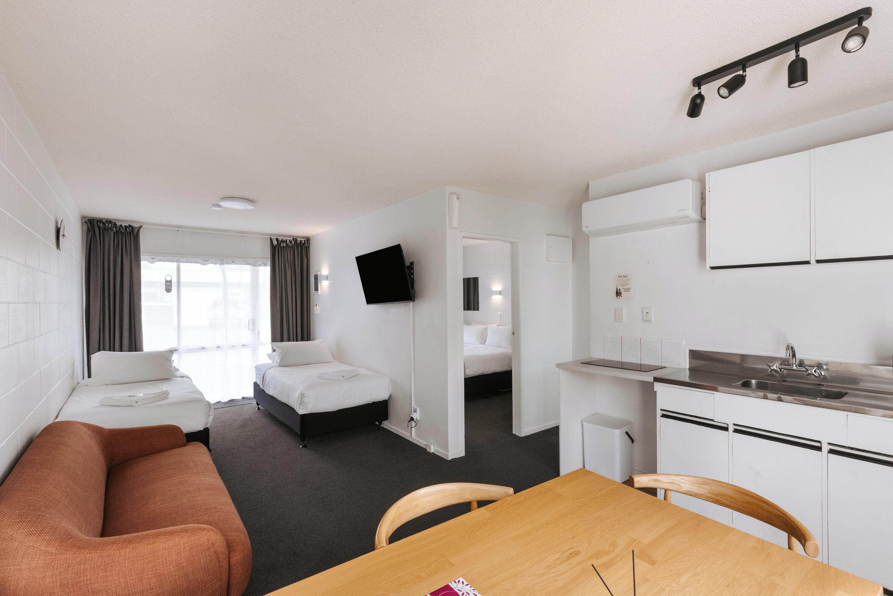 Habitación de hotel con cama, sofá, mesa de comedor, zona de cocina y televisor montado en la pared.