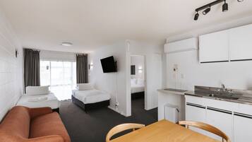 Habitación de hotel con cama, sofá, mesa de comedor, zona de cocina y televisor montado en la pared.