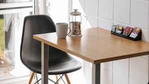 A table with a coffee pot, a mug, and a magazine rack. - Roselands Motel (Tauranga)