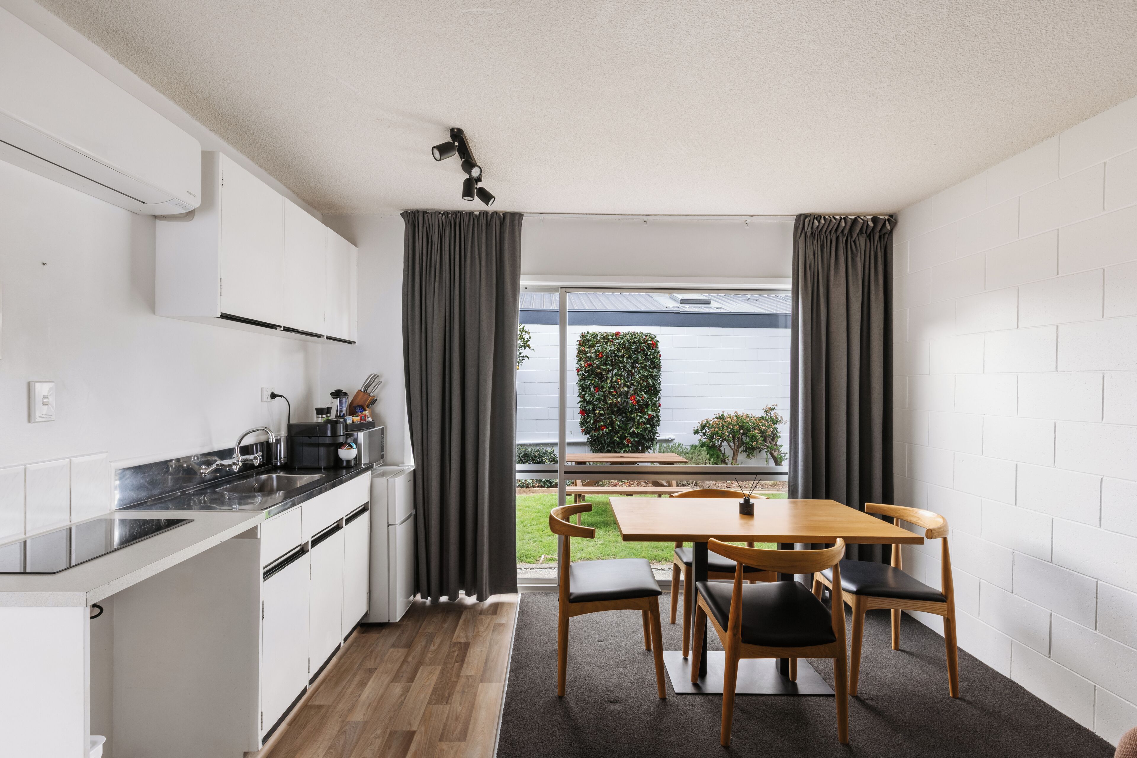 A compact kitchen with a dining area, a view of a garden, and a white brick wall.