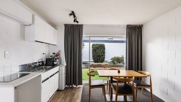 A compact kitchen with a dining area, a view of a garden, and a white brick wall.